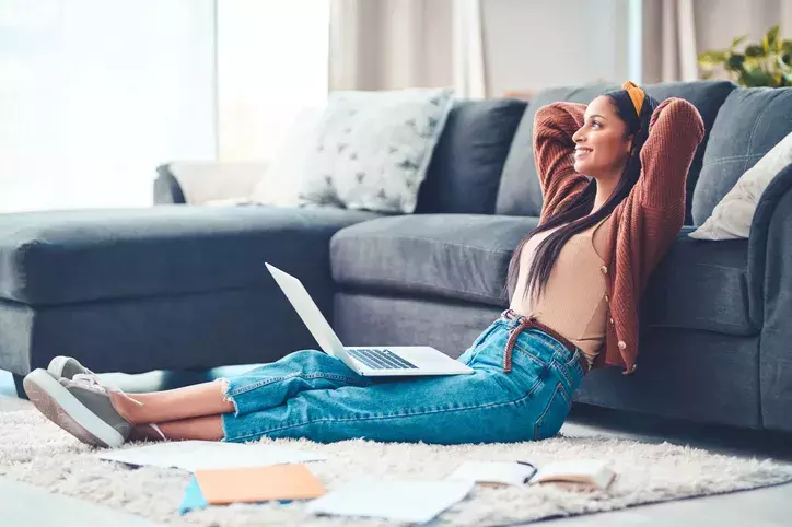 happy woman leaning against couch with laptop