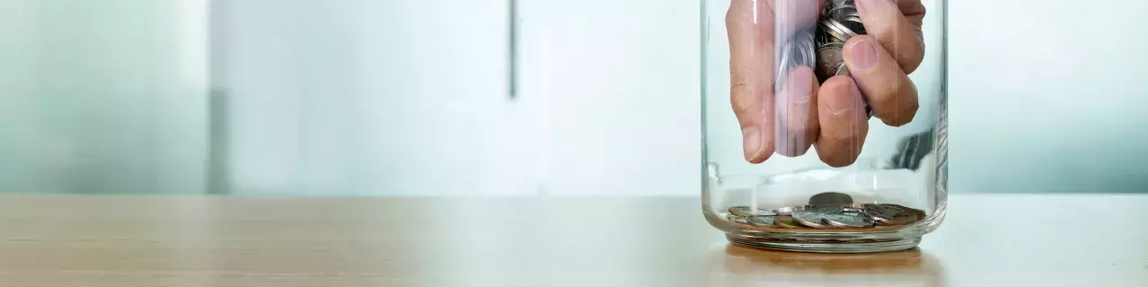 A hand reaching into a jar and taking coins.