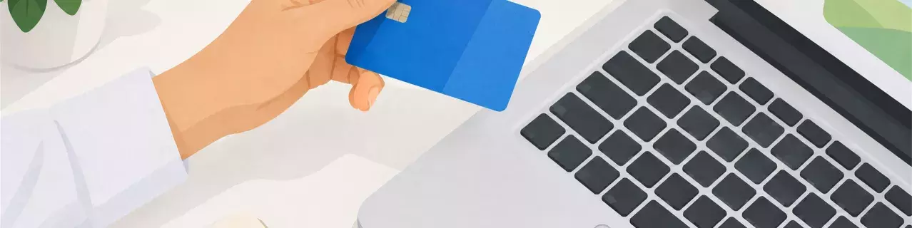 Hand holding blue bank card beside laptop