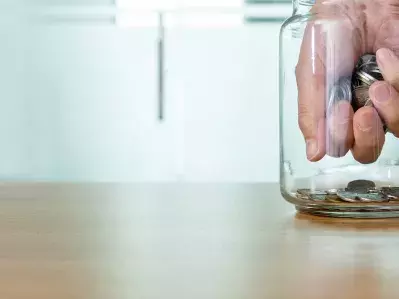 A hand reaching into a jar and taking coins.