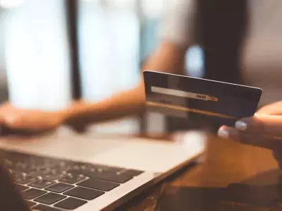 A person working at their laptop holding a credit card
