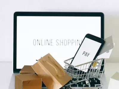 A laptop with a tiny shopping cart, boxes, and a phone