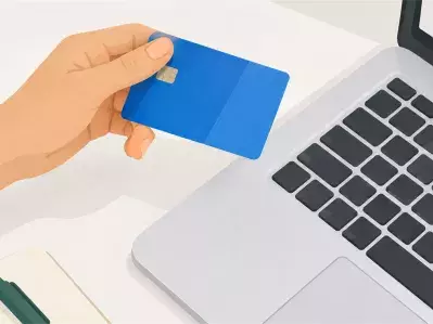 Hand holding blue bank card beside laptop